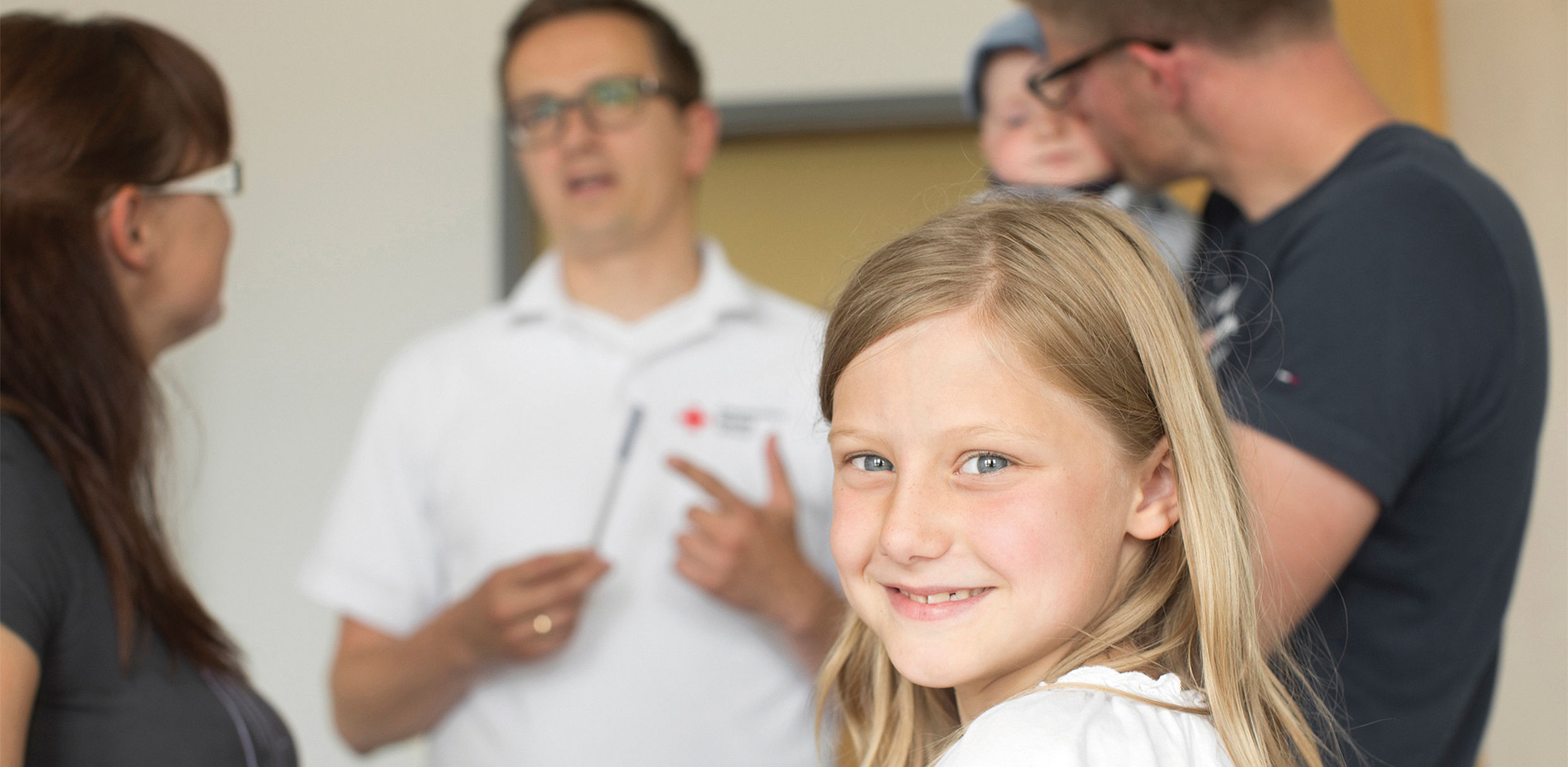 Mutter und Kind DRK-KV Dresden e.V - mehrere Personen im Gespräch mit einem Berater - blondes Mädchen lächelt in die Kamera (Nahaufnahme) 