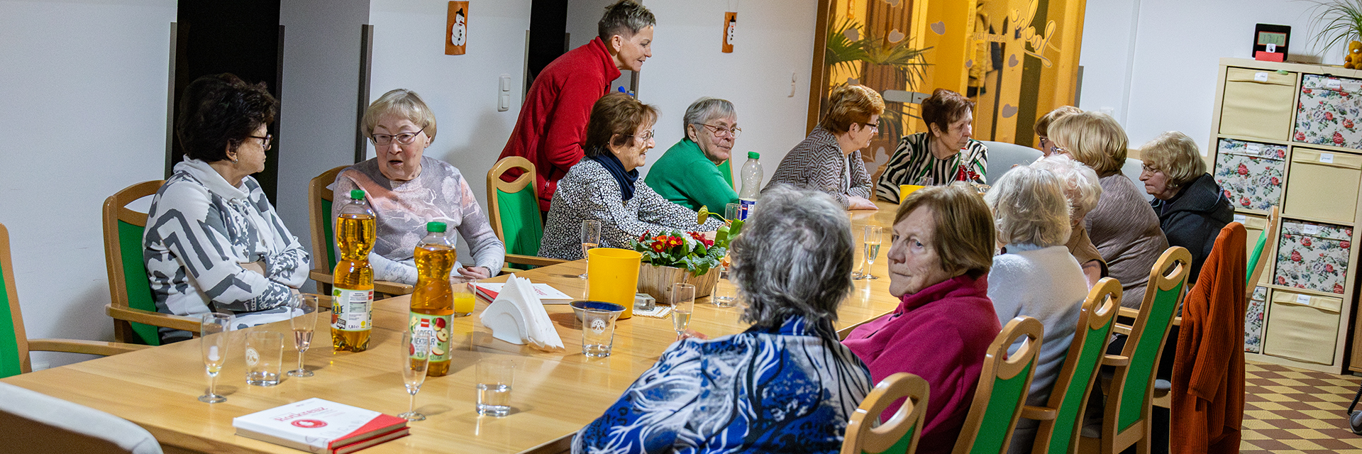 Eine Gruppe von Senioren sitzen gemeinsam an einem langen Tisch und unterhalten sich.