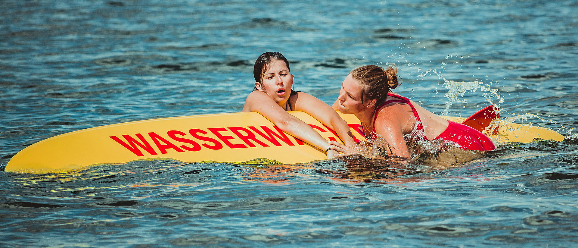 Helferin mit geretteter Schwimmerin auf dem Rettungsbrett im Wasser