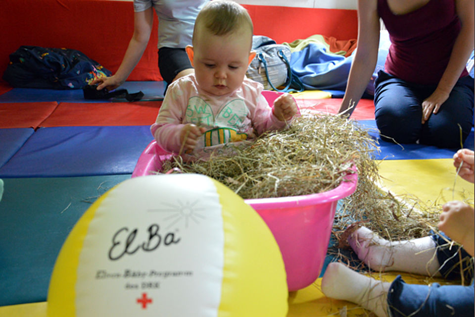 Ein Baby spielt mit heut. Im Vordergrund ein Wasserball mit dem ElBa-Logo.