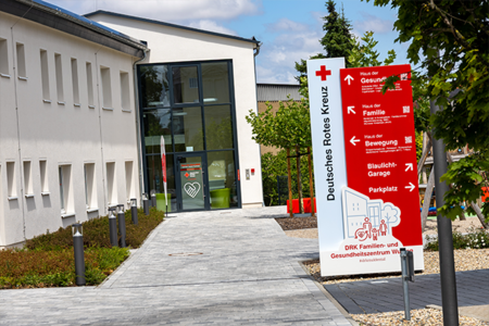 Der Eingangsbereich des DRK Familien- und Gesundheitszentrums Wurzen, gekennzeichnet durch eine große rot-weiße Hinweistafel mit Wegweisern.