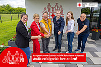 Sechs Personen stehen lächelnd vor einem Gebäude des DRK Kreisverbandes Muldental e.V. und zeigen mit den Daumen nach oben, um das erfolgreich bestandene Audit des DRK-Fahrdienstes zu feiern. Im Vordergrund befindet sich ein roter Kreis mit dem weißen Logo 'Wir machen MOBIL' und im unteren Bereich ein roter Textbalken mit der Aufschrift: 'Ausgezeichnete Qualität im DRK-Fahrdienst Muldental! Audit erfolgreich bestanden!