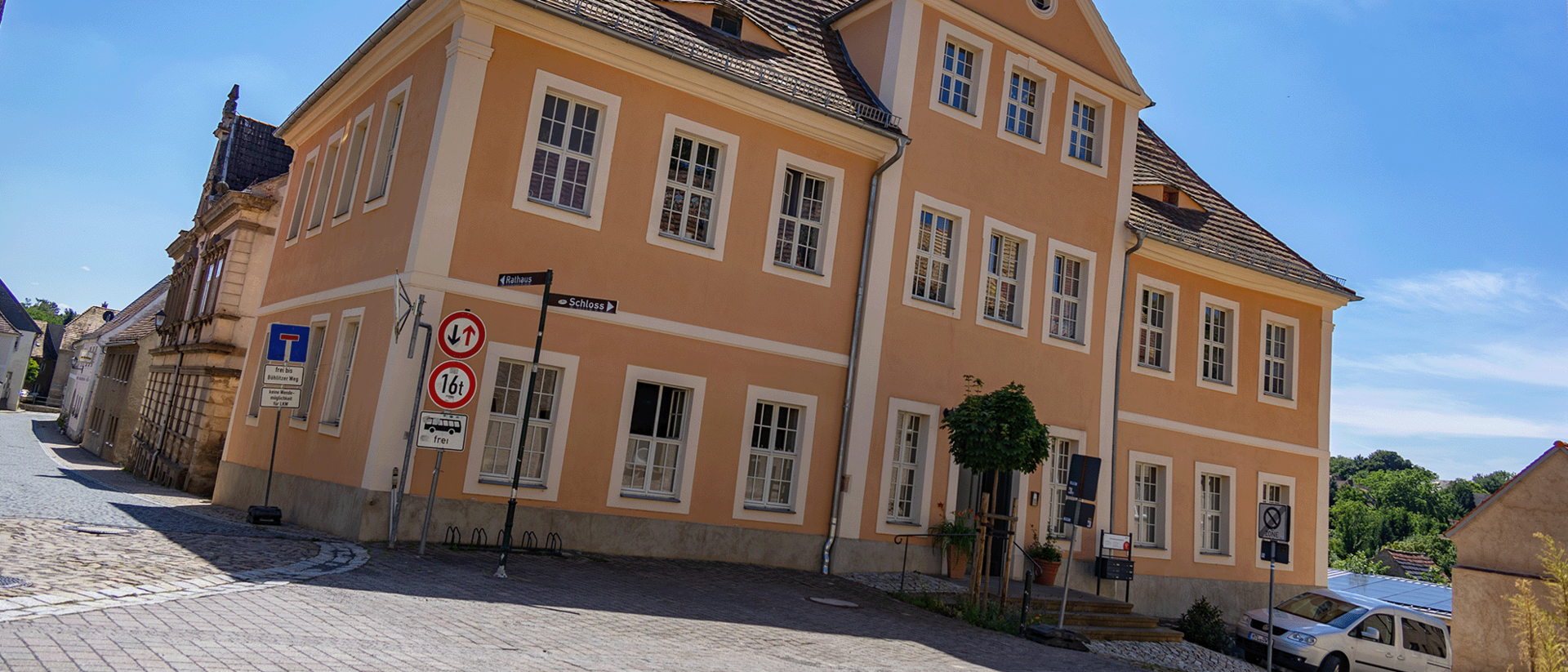 PT-Praxis Mutzschen Außsenansicht Straßenansicht eines historischen, pfirsichfarbenen Gebäudes mit Sprossenfenstern und Satteldach an einem sonnigen Tag.