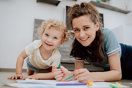 Mutter liegt mit ihrer Tochter im Vorschulalter auf dem Boden und zeichnet gemeinsam.