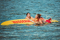 Helferin mit geretteter Schwimmerin auf dem Rettungsbrett im Wasser