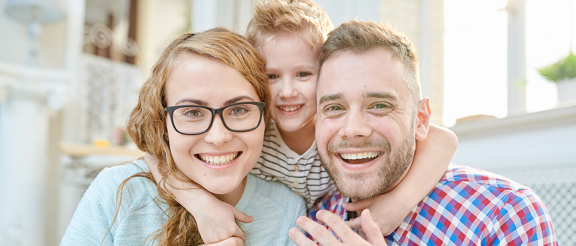 Familienbild Vater, Mutter und Kind kuscheln und lächeln in die Kamera.