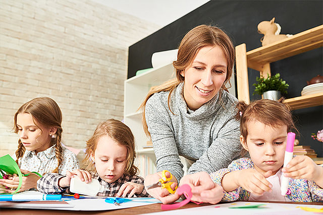 Eine Frau bastelt mir drei Kindern gemeinsam an einem Tisch.